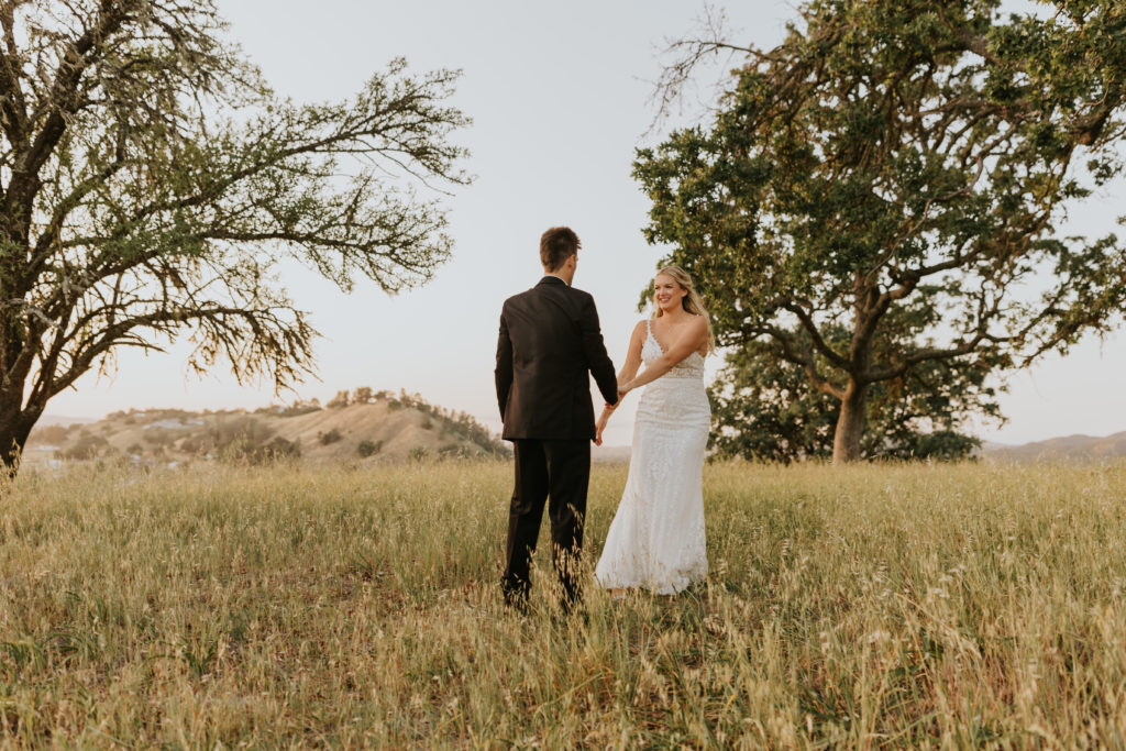 Bride and groom going through a field on the hills of Paso Robles CA winecountry at the Grace Maralyn Estate