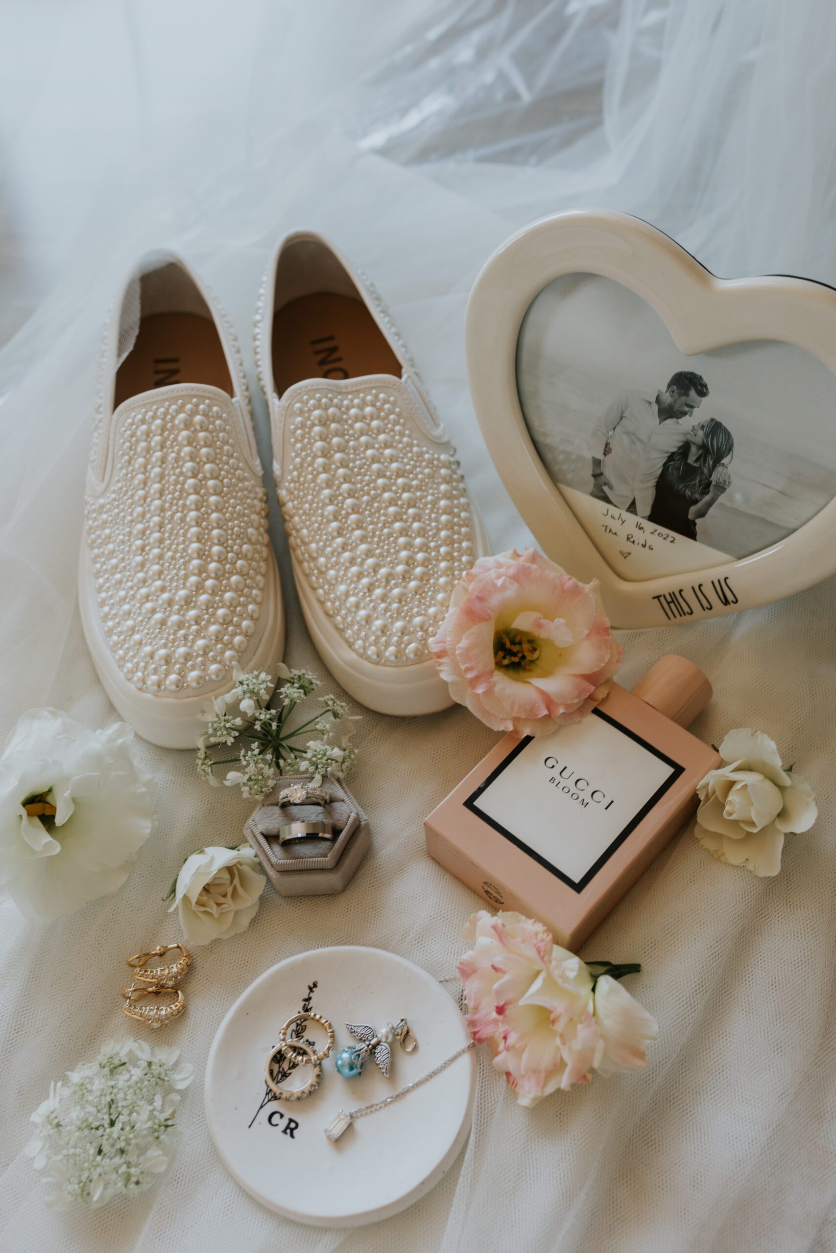 Wedding flat lay photograph featuring the bride's shoes, a picture frame, perfume, rings, earrings, and flowers