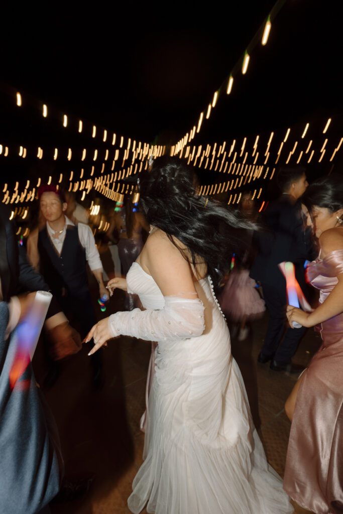 High-energy dance floor moment with the bride and guests partying under flash at a modern wedding reception.
