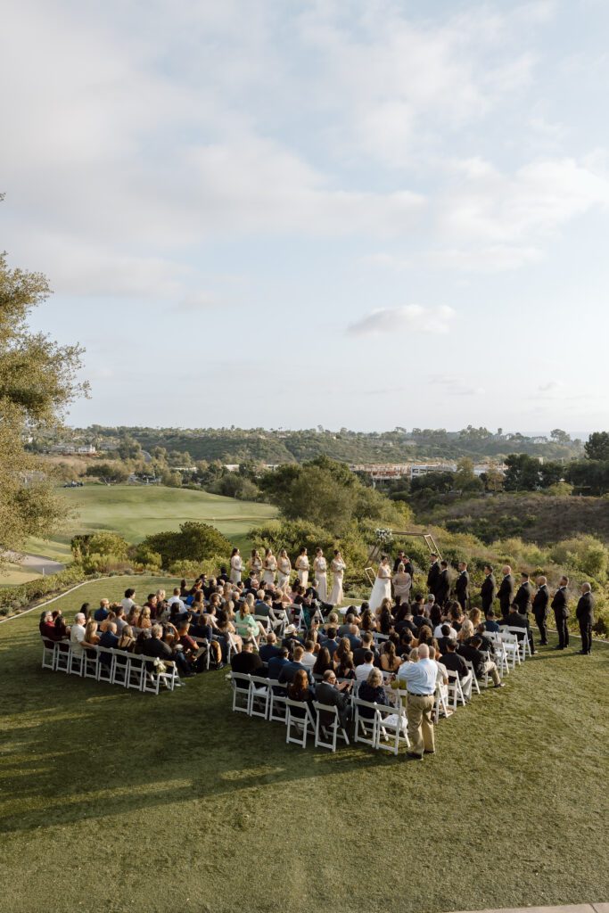 An outdoor wedding ceremony at a beautiful golf course in Southern California, with rolling hills and blue skies.
