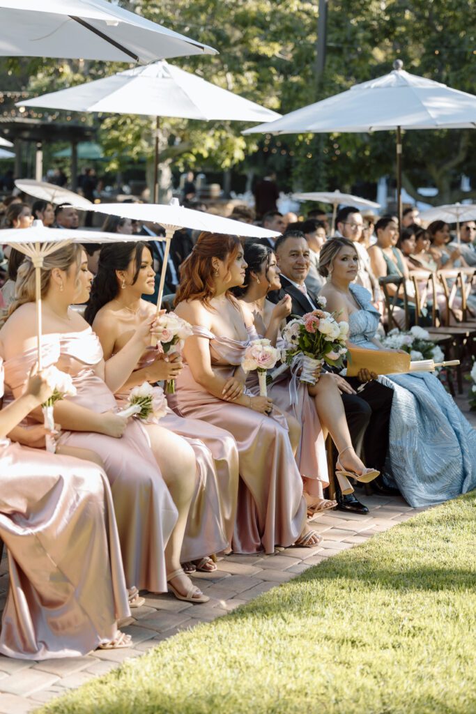 Guests and bridesmaids hold parasols to keep cool during a hot summer wedding in Southern California, photographed by Laura Burns Photography.