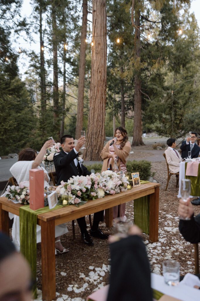 Newlyweds raise their champagne glasses following a speech given by the maid of honor during an outdoor wedding ceremony in a Redwoods grove in Southern California.