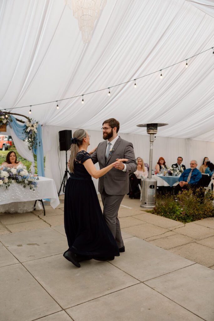 As the groom and his mother share their mother-daughter dance, guests sit near space heaters to keep warm during an outdoor wedding in Southern California.