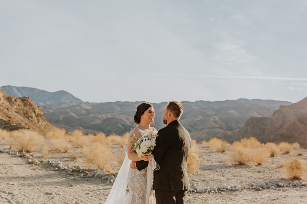 Bride and Groom are looking at each other with their arms around each other for their outdoor elopement in the desert of Southern California