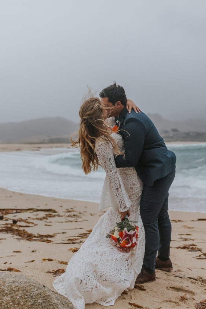 Cute couple kissing on the beach with rain in the background.
